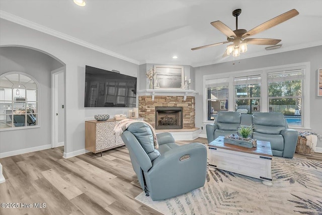 living room with ceiling fan, ornamental molding, a stone fireplace, and light hardwood / wood-style flooring