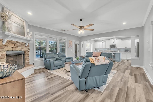 living room with ornamental molding, ceiling fan, a fireplace, and light hardwood / wood-style floors