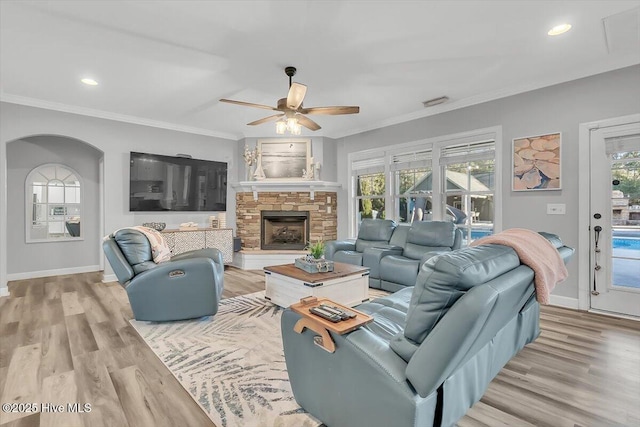 living room with crown molding, a stone fireplace, ceiling fan, and light hardwood / wood-style flooring