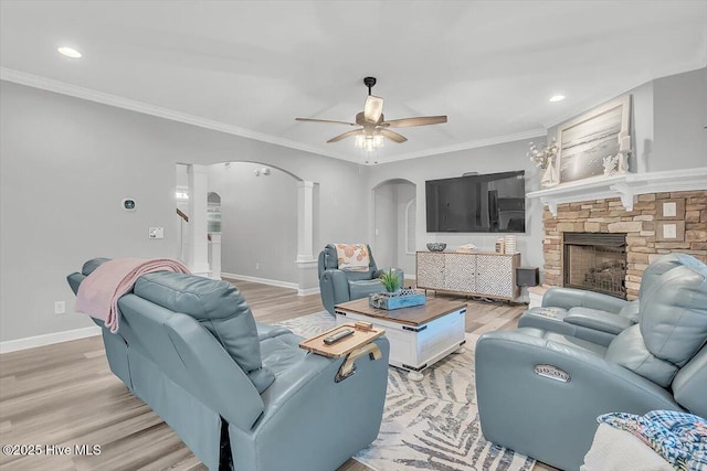 living room with a fireplace, wood-type flooring, ornamental molding, and ceiling fan