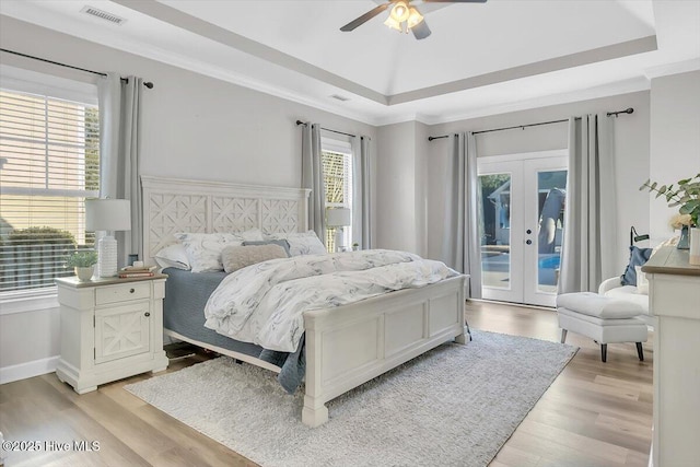 bedroom featuring access to outside, light hardwood / wood-style floors, a raised ceiling, crown molding, and french doors