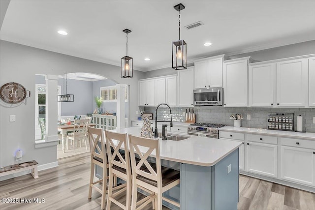 kitchen with sink, appliances with stainless steel finishes, hanging light fixtures, an island with sink, and white cabinets