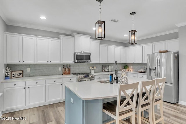 kitchen with sink, hanging light fixtures, stainless steel appliances, white cabinets, and a center island with sink