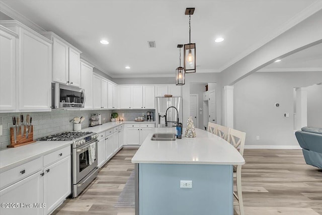 kitchen with sink, appliances with stainless steel finishes, a kitchen island with sink, a kitchen breakfast bar, and white cabinets