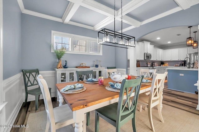 dining area featuring ornamental molding, coffered ceiling, a notable chandelier, beam ceiling, and light hardwood / wood-style flooring