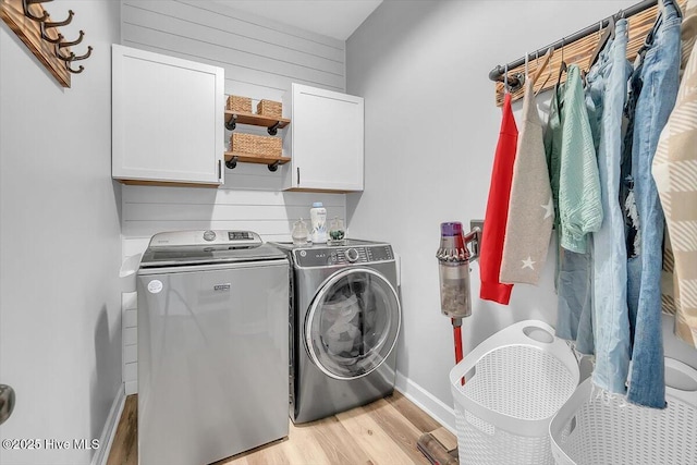 laundry area featuring cabinets, washing machine and dryer, wooden walls, and light wood-type flooring