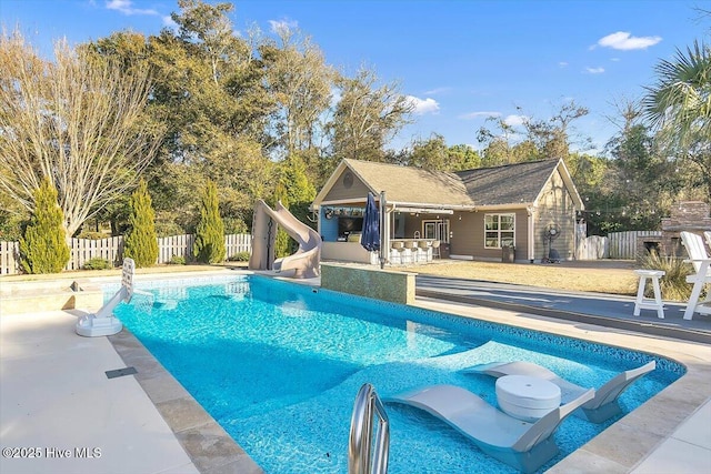 view of pool featuring an outbuilding, a water slide, exterior bar, and a patio