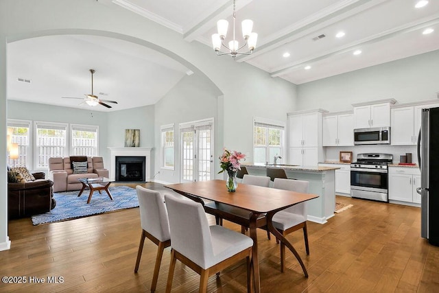 dining area featuring beamed ceiling, a towering ceiling, ceiling fan with notable chandelier, and light hardwood / wood-style flooring