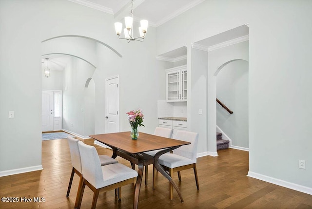 dining space featuring dark wood-type flooring, a towering ceiling, crown molding, and an inviting chandelier