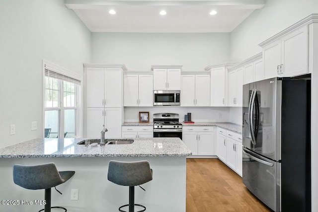 kitchen with appliances with stainless steel finishes, a high ceiling, light stone countertops, white cabinets, and a kitchen bar