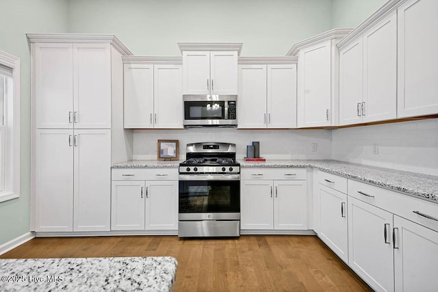 kitchen featuring appliances with stainless steel finishes, white cabinetry, backsplash, light stone countertops, and light wood-type flooring