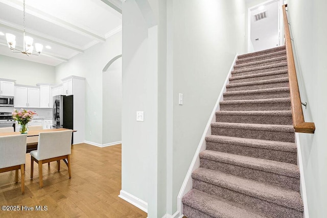 stairway with beam ceiling, a notable chandelier, and hardwood / wood-style flooring