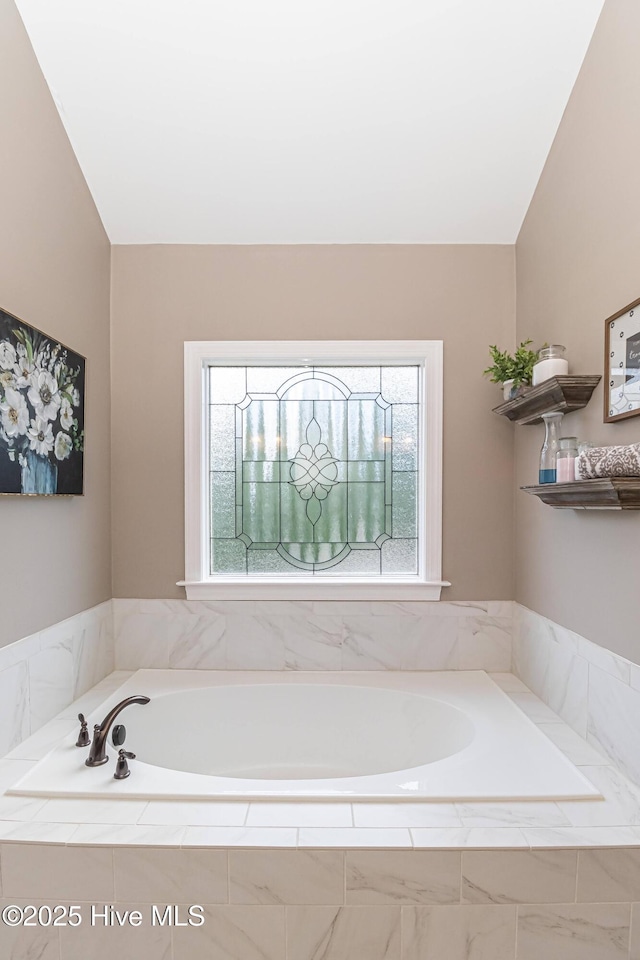 bathroom with lofted ceiling and tiled bath