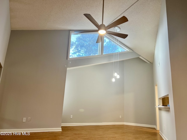 empty room with ceiling fan, wood-type flooring, high vaulted ceiling, and a textured ceiling