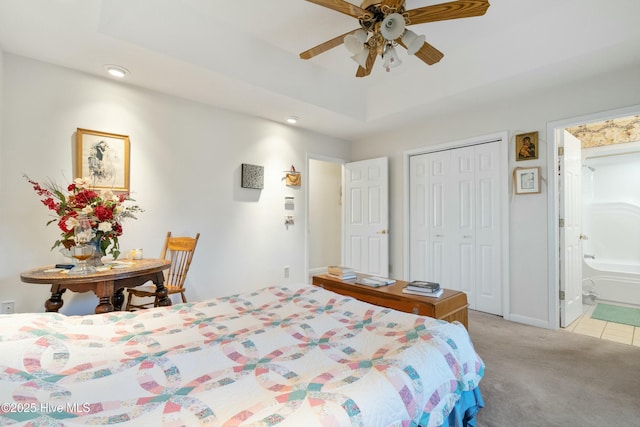 carpeted bedroom with ceiling fan, connected bathroom, a tray ceiling, and a closet