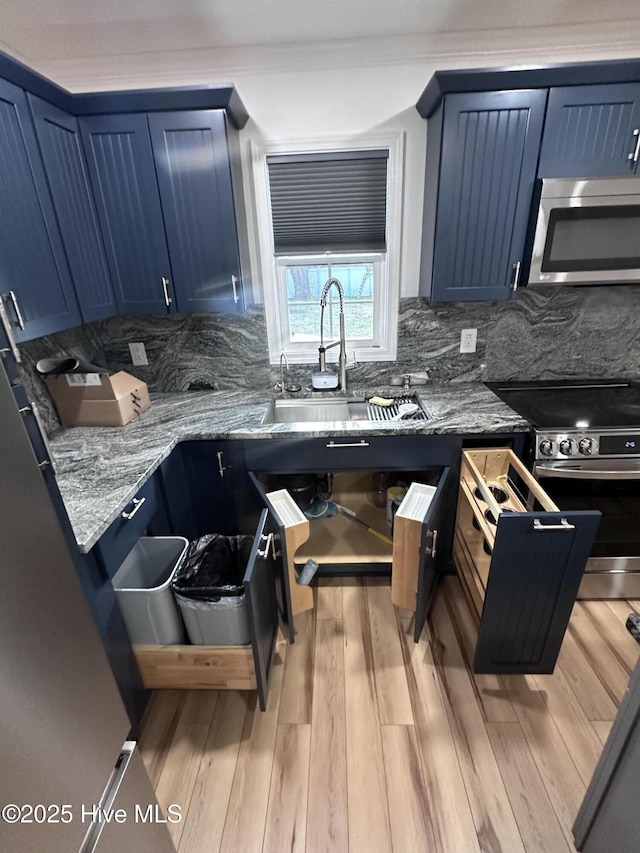 kitchen featuring blue cabinetry, sink, light hardwood / wood-style flooring, stainless steel appliances, and decorative backsplash