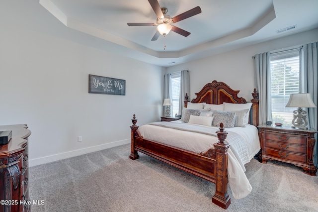 bedroom featuring a raised ceiling, ceiling fan, carpet flooring, and multiple windows