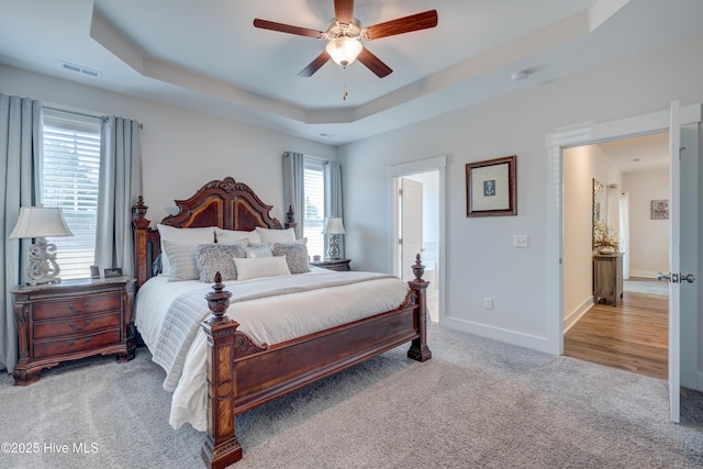 carpeted bedroom with a raised ceiling and ceiling fan