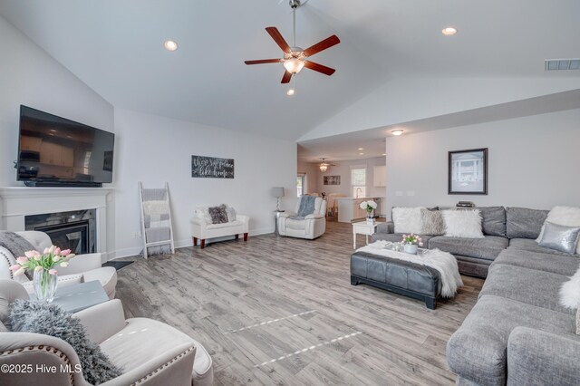 living room with ceiling fan, high vaulted ceiling, a fireplace, and light hardwood / wood-style flooring