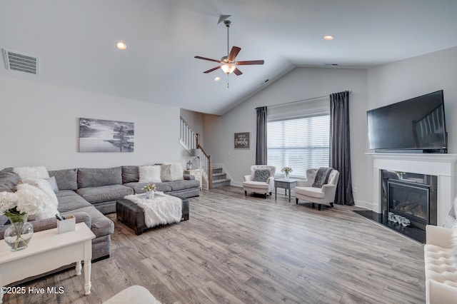 living room with vaulted ceiling, a high end fireplace, ceiling fan, and light wood-type flooring