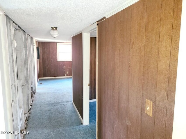 corridor featuring wood walls, carpet, and a textured ceiling