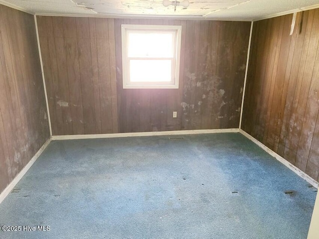 carpeted spare room with baseboards, ornamental molding, and wooden walls