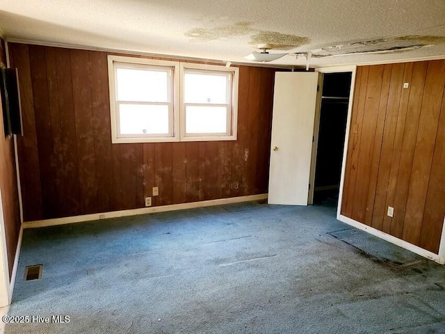 carpeted spare room featuring wood walls, baseboards, visible vents, and a textured ceiling