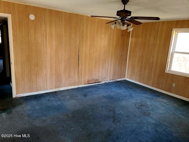 spare room with a textured ceiling, dark colored carpet, wood walls, and ceiling fan