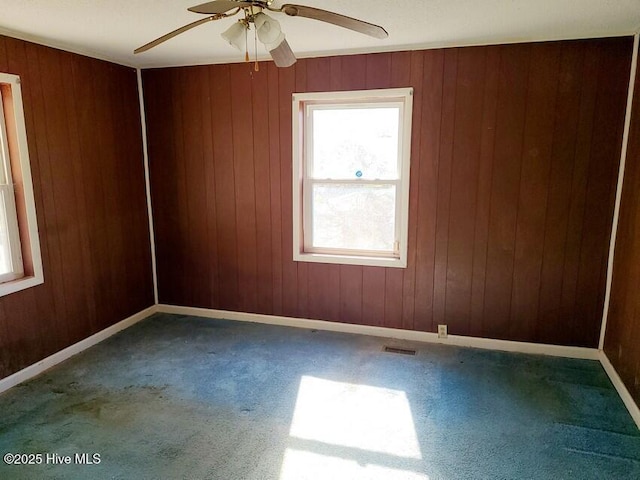 empty room featuring baseboards, visible vents, wooden walls, and carpet flooring