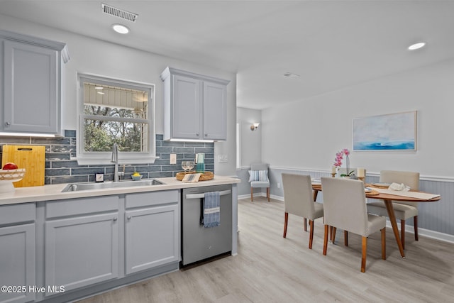 kitchen featuring stainless steel dishwasher, sink, light hardwood / wood-style flooring, and gray cabinetry