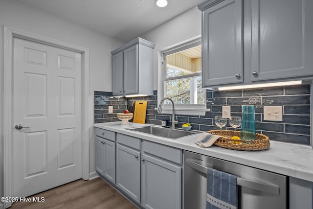 kitchen featuring sink, dark wood-type flooring, gray cabinets, tasteful backsplash, and stainless steel dishwasher