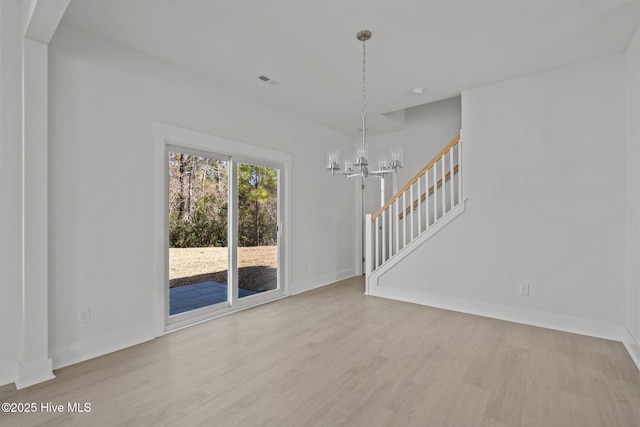 empty room with light wood-type flooring and a notable chandelier