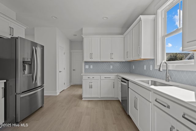 kitchen featuring appliances with stainless steel finishes, tasteful backsplash, white cabinetry, sink, and light hardwood / wood-style flooring