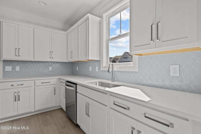 kitchen with sink, backsplash, white cabinets, stainless steel dishwasher, and light wood-type flooring