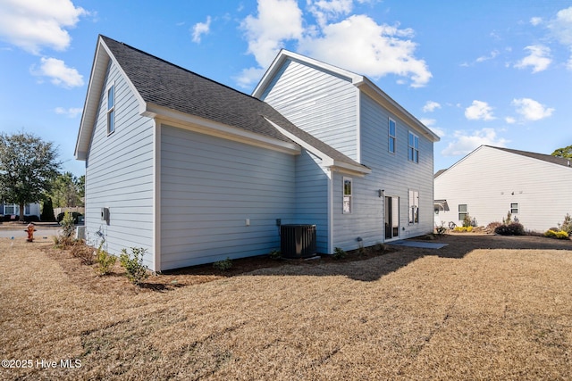 rear view of house featuring central AC unit and a lawn