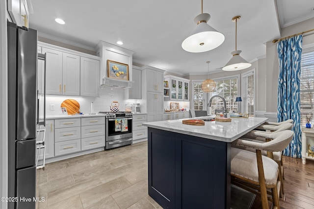 kitchen featuring white cabinetry, hanging light fixtures, ornamental molding, an island with sink, and stainless steel appliances