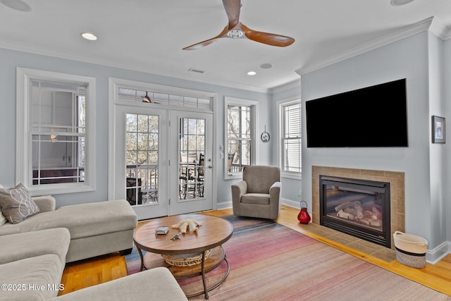 living room with a tiled fireplace, crown molding, hardwood / wood-style floors, and ceiling fan