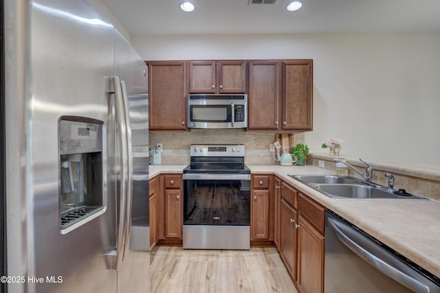 kitchen with appliances with stainless steel finishes, sink, light wood-type flooring, and decorative backsplash