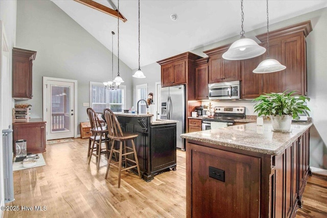 kitchen featuring light hardwood / wood-style flooring, a breakfast bar, hanging light fixtures, stainless steel appliances, and light stone countertops