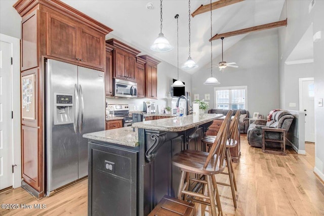 kitchen featuring appliances with stainless steel finishes, pendant lighting, an island with sink, a kitchen breakfast bar, and light wood-type flooring