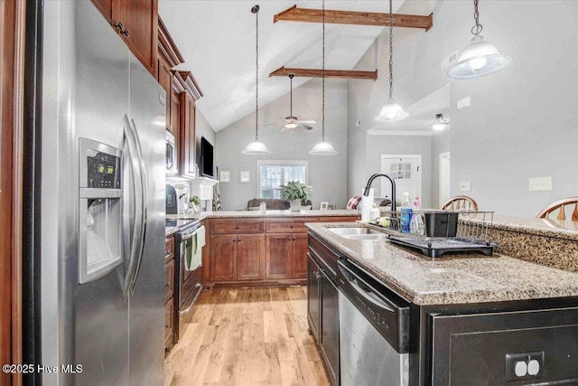 kitchen with sink, light hardwood / wood-style flooring, pendant lighting, stainless steel appliances, and a kitchen island with sink