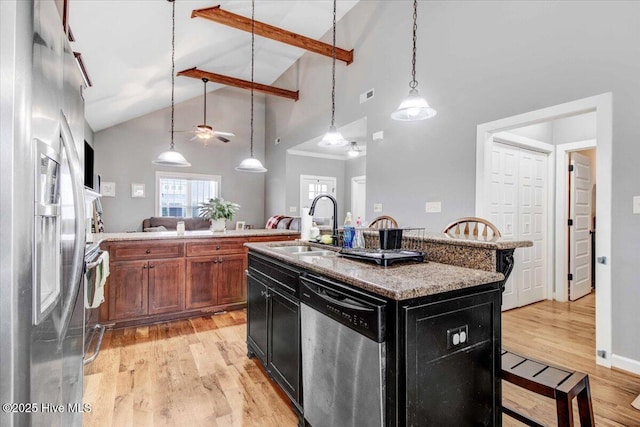 kitchen with a kitchen island with sink, stainless steel appliances, light stone counters, a kitchen bar, and decorative light fixtures