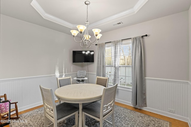 dining area featuring an inviting chandelier, hardwood / wood-style floors, ornamental molding, and a raised ceiling