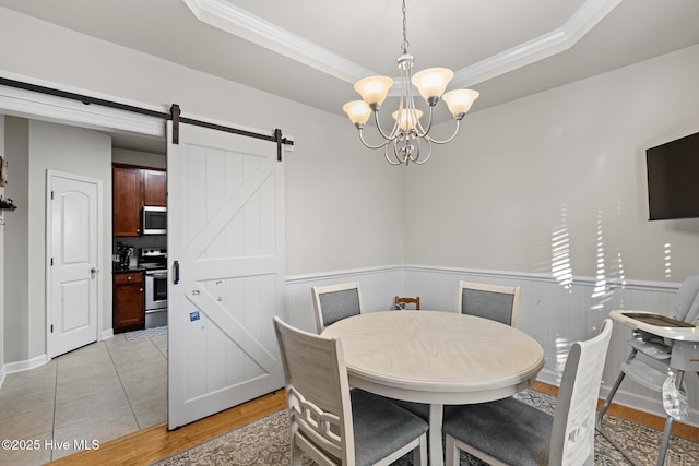 tiled dining area with an inviting chandelier, a tray ceiling, ornamental molding, and a barn door