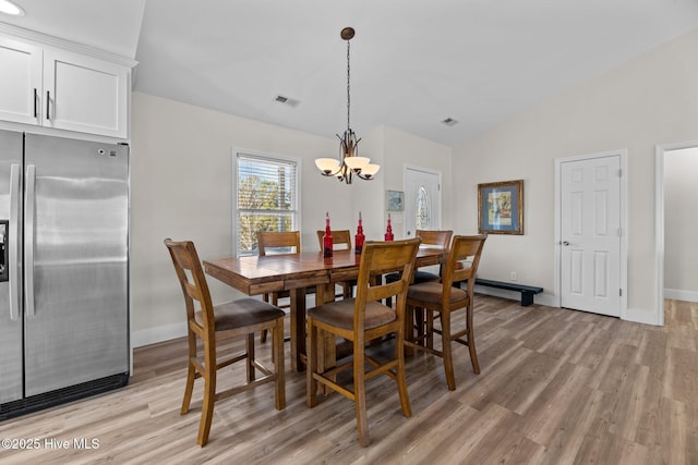 dining area with an inviting chandelier, vaulted ceiling, and light wood-type flooring