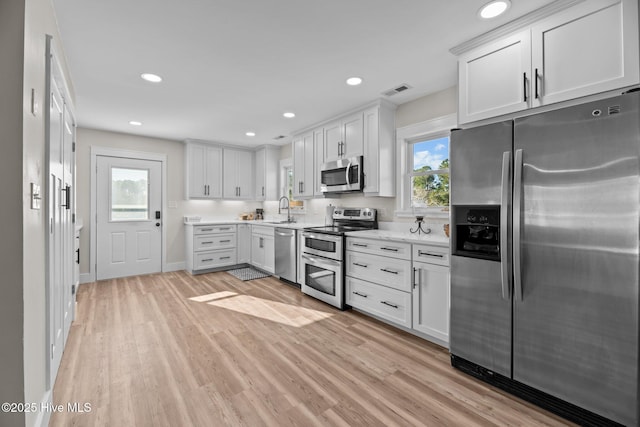 kitchen with sink, plenty of natural light, appliances with stainless steel finishes, light hardwood / wood-style floors, and white cabinets