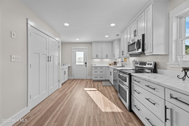 kitchen featuring sink, light hardwood / wood-style flooring, stainless steel appliances, light stone counters, and white cabinets