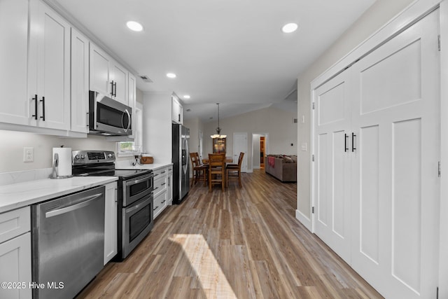 kitchen featuring white cabinetry, appliances with stainless steel finishes, lofted ceiling, and light stone counters