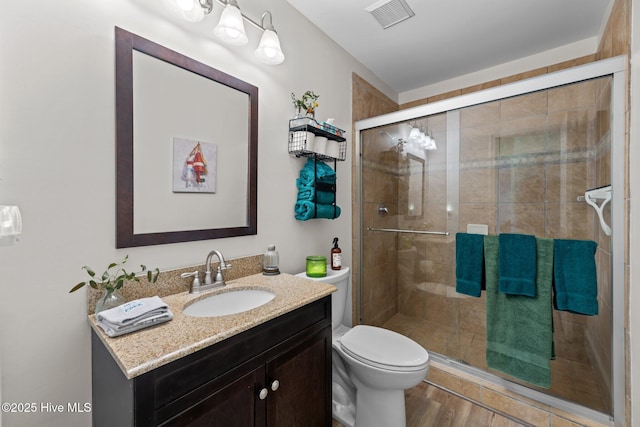 bathroom with toilet, wood-type flooring, vanity, and a shower with shower door