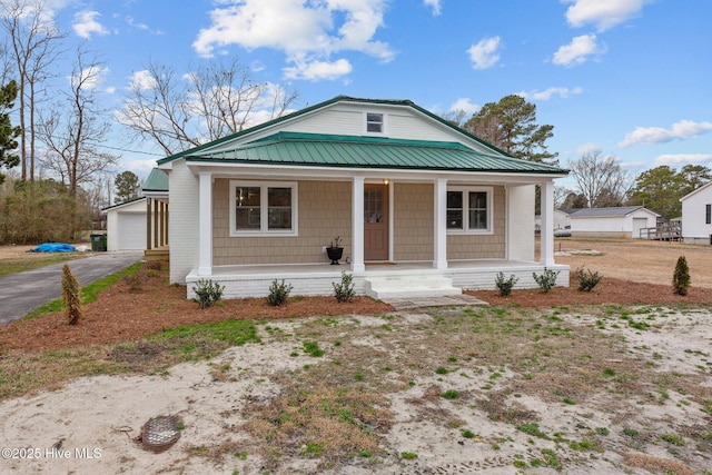 bungalow-style house featuring a garage, metal roof, a porch, and an outbuilding